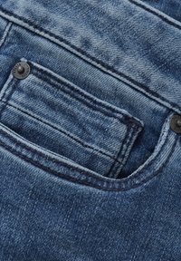 Zbliżenie kieszeni dżinsowych spodni. Niebieska tkanina o wypłowiałej fakturze. Charakterystyczne przeszycia i czarny guzik na kieszeni.