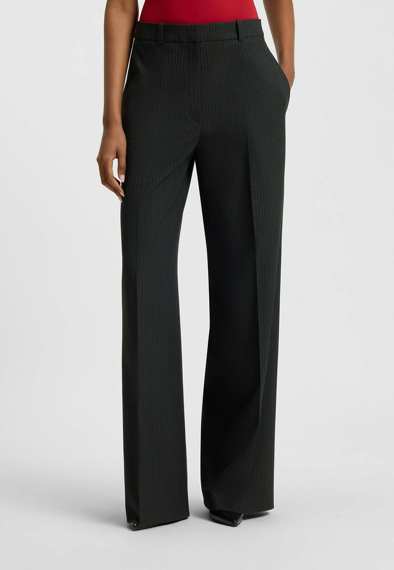 Pantaloni a gamba larga a righe nere con una texture liscia, caratterizzati da vita media e tasche laterali. Design su misura con linee pulite.