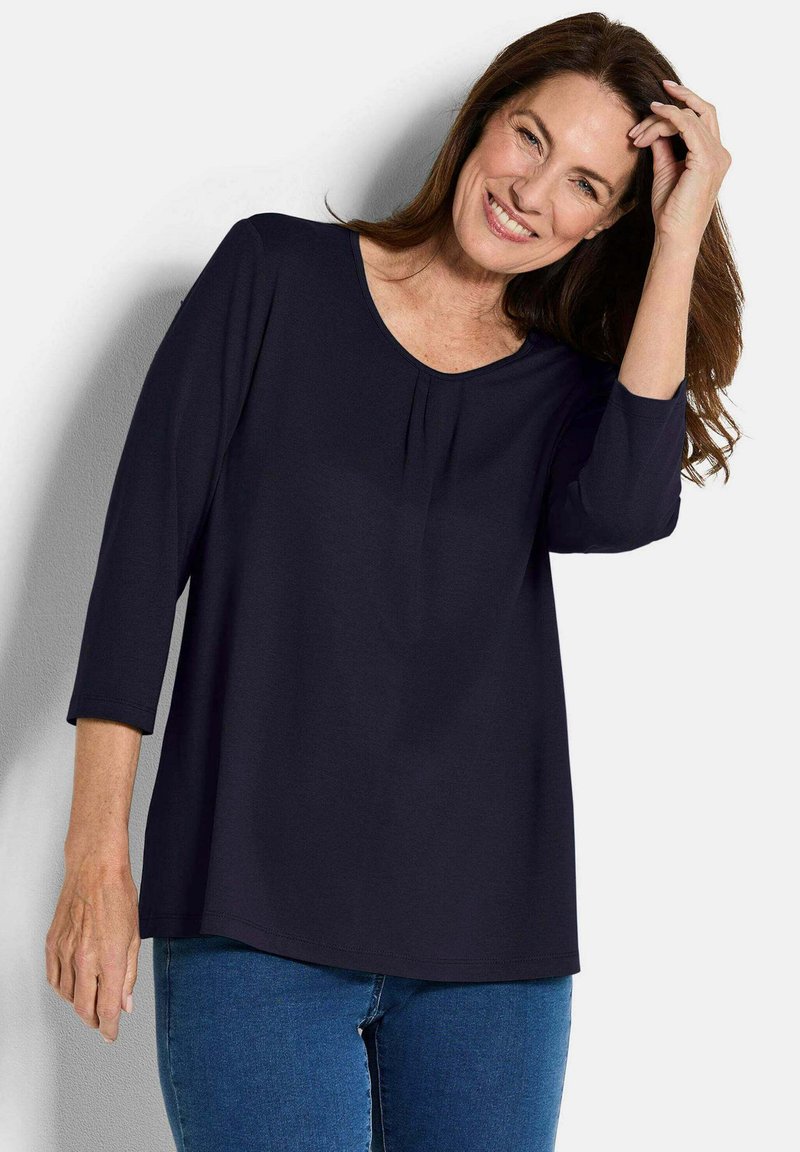 Marineblaues Oberteil mit Dreiviertelärmeln, rundem Halsausschnitt und subtilen Falten am Vorderteil. Leichter Stoff, lockere Passform und weiche Textur.