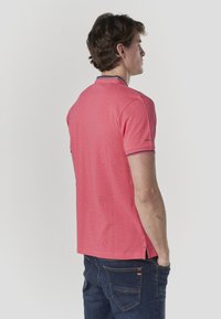 Rosa Poloshirt mit kurzen Ärmeln, versehen mit kleinen blauen und weißen Mustern, kontrastierendem Kragenbesatz und Seitenschlitzen für mehr Komfort.