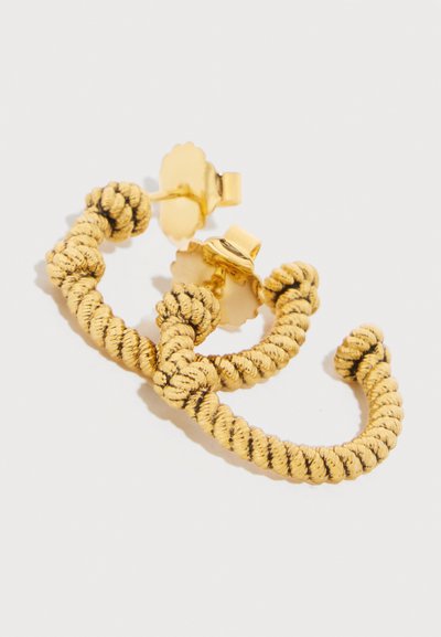 Σκουλαρίκια κρίκοι με υφή στριφογυρισμένου σχοινιού σε χρυσό τόνο, με πίσω μέρος για καρφί και κούμπωμα πεταλούδας, πάνω σε απλό ανοιχτό φόντο.