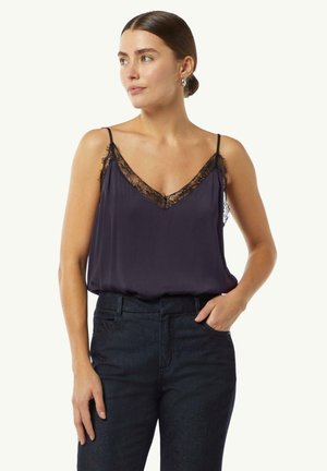 Satin camisole in navy with a deep V-neck and black lace trim along the neckline and hem. Thin adjustable straps. Paired with dark jeans.