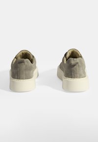 Gray suede sneakers with a padded ankle, cream-colored rubber sole, and a minimalistic design. Textured upper with contrasting stitching detail.