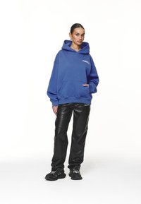 Oversized blue hoodie with a front pocket and logo. Paired with black faux leather pants and black sneakers featuring white accents.