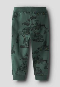 Zaļas kokvilnas sporta bikses ar melnu grafiku, kur redzamas celtniecības tehnikas. Elastīga josta un manšetes nodrošina ciešu piegulumu.