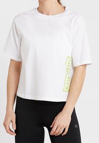 Camiseta corta blanca de algodón, con mangas cortas y un logo en neón amarillo "CALVIN KLEIN" en el lateral.