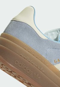 Adidas sneakers met een combinatie van lichtblauw suede en crèmekleurig leer, voorzien van een gumrubberen zool. Gouden merktekens aan de zijkant.