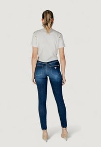 White t-shirt with button accents on shoulders, paired with dark blue skinny jeans. Clear stitching and back pockets visible.
