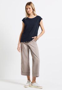 Lahti lyhythihainen t-paita, jossa on pyöreä kaula-aukko, yhdistettynä beigeihin leveälahkeisiin housuihin ja valkoisiin lenkkareihin, luoden rentoa asustetta.