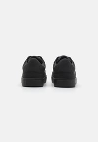 Sneakers neri realizzati in materiale sintetico, caratterizzati da un design a bassa altezza, punta arrotondata e suola in gomma testurizzata con dettagli minimi.