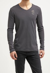 Gray long-sleeve T-shirt with a V-neck, made from smooth fabric; features a small logo on the chest and a fitted design.