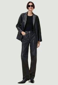 Μαύρο δερμάτινο σακάκι με μετρημένα κεντήματα, συνδυασμένο με αντίστοιχες δερμάτινες παντελόνες υψηλής μέσης και μαύρες ψηλές μπότες. Υφή με εφαρμοστό σχέδιο.