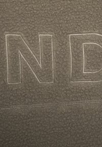 Braune Fleece-Decke mit strukturierter Oberfläche und eingeprägten Buchstaben, versehen mit einer abgesteppten Kante für Langlebigkeit und einem weichen, warmen Erscheinungsbild.