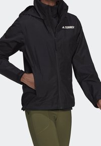 Svart lättviktsjacka med hel dragkedja, justerbar huva och elastiska ärmslut. Har "TERREX"-logotypen på bröstet och sidofickor.