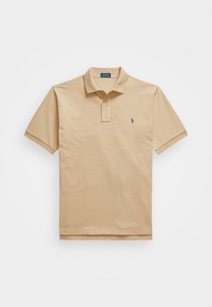 Beige kokvilnas polo krekls ar īsām piedurknēm, ar trīs pogu aizdari un nelielu zilu logo kreisajā krūtī. Gluda tekstūra.