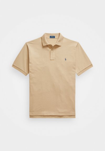 Camisa polo de algodão bege com mangas curtas, apresentando uma abertura de três botões e um pequeno logotipo azul no lado esquerdo do peito. Textura suave.