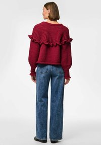Suéter de punto burdeos con un dobladillo con volantes y mangas anchas, combinado con unos jeans de pierna recta de talle alto en azul y botas negras de tobillo.