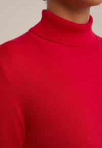 Pull à col roulé rouge avec une texture lisse et côtelée, au design ajusté. Il présente un col haut et des détails d'épaules sans couture.