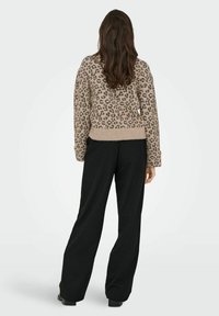 Løveprint sweater i beige nuancer, med ribbet kant og manchetter, båret med sorte vide bukser. Blød tekstur, afslappet pasform.