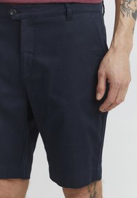 Shorts bleu marine en tissu texturé, dotés d'une fermeture à bouton, de poches latérales et d'un ourlet droit avec une finition soignée.