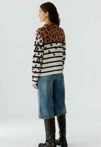 Pull en maille avec un motif léopard marron sur les épaules et un corps à rayures bleu marine, associé à un denim à jambes larges et des bottes noires au genou.