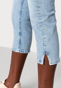 Vaaleansininen farkkukaprit, joissa on raaka helma ja sivuhalkiot lahkeissa. Materiaali näyttää pehmeältä ja siinä on hieman haalistunut pinta.