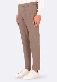 Chinos beige con pieghe frontali, gamba affusolata e tasche laterali, abbinati a sneaker bianche. Tessuto liscio, design casual.