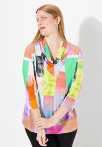 Camiseta de manga larga colorida con cuello drapeado, hecha de una tela ligera. El diseño incluye patrones geométricos en tonos vibrantes como verde, naranja y rosa.