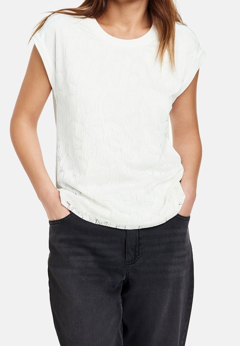 Top blanco de manga corta con un patrón texturizado, escote redondo y corte relajado, combinado con pantalones de mezclilla negros.