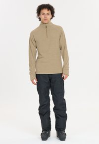 Beige langærmet zip-up trøje med høj krave, parret med sorte vandtætte bukser og skistøvler, designet til udendørs aktiviteter.