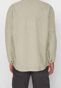 Jasnozielona koszula ze sztruksu z długimi rękawami, mankietami na guziki i prostym krojem. Posiada fakturowany prążkowany wzór oraz boczne rozcięcia.