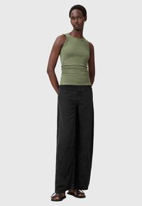 Top de tirantes en verde oliva con una silueta ajustada, combinado con pantalones anchos negros de pierna suelta y sandalias negras con un acento decorativo.