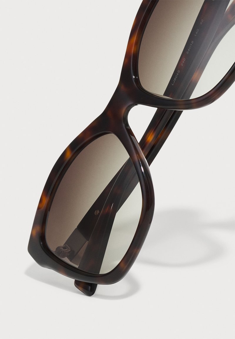 Schildpatt-Sonnenbrille mit übergroßen quadratischen Rahmen, braunen Verlaufslinsen und Metallakzenten an den Scharnieren. Glatte Acetat-Oberfläche.