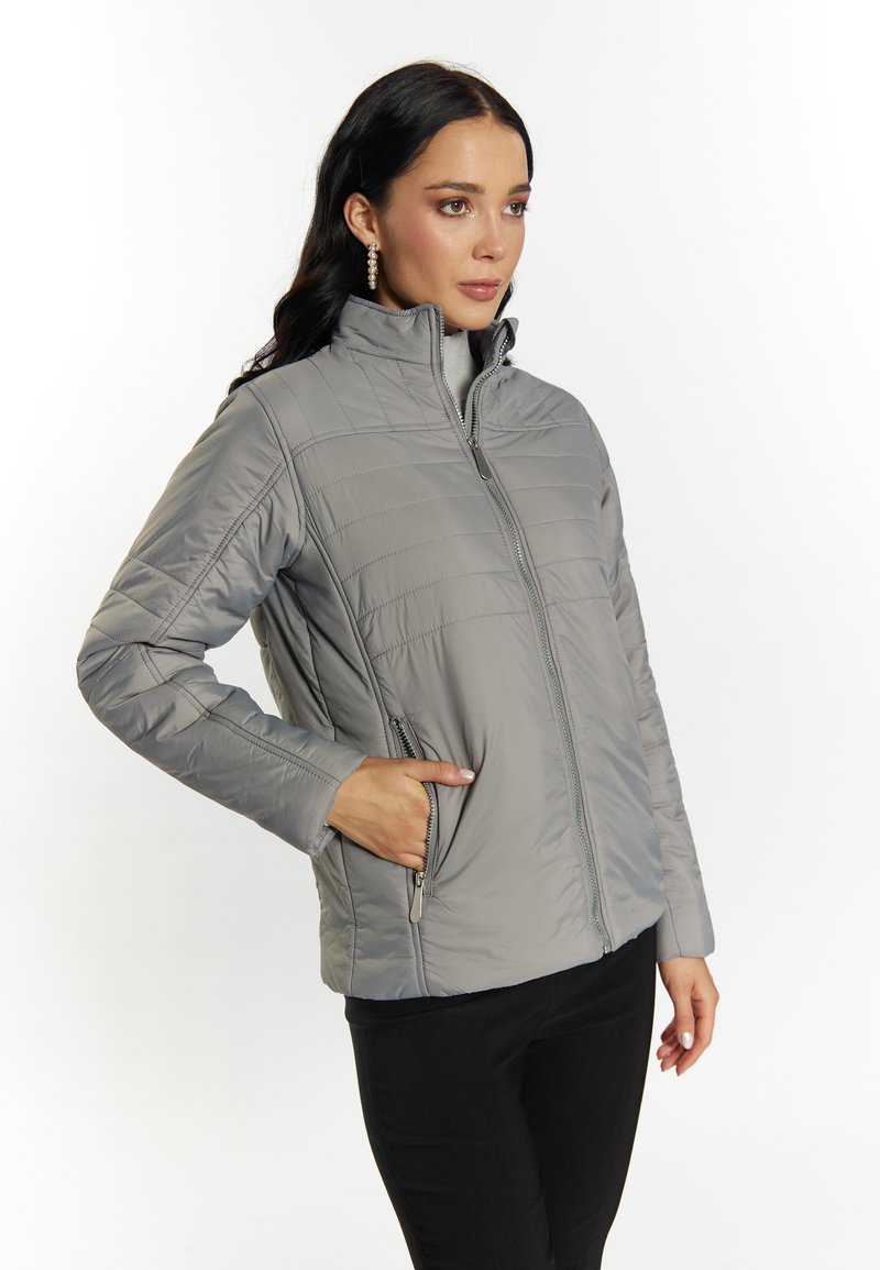 Chaqueta aislante gris con cierre de cremallera en el frente, cuello alto y bolsillos laterales. Presenta un patrón de acolchado horizontal y una textura suave.