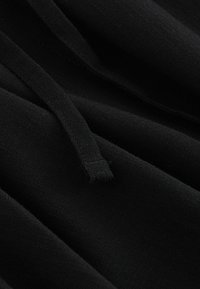 Tessuto nero con una consistenza morbida e liscia; presenta un dettaglio con coulisse. Il materiale si drappeggia aderente con cuciture e pieghe visibili.