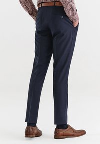 Granatowe, dopasowane spodnie z subtelnym wzorem w kratę, z bocznymi kieszeniami i kieszenią na plecach. Brązowe skórzane buty.