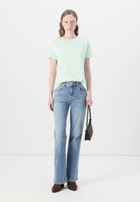 Lys grønn kortermet t-skjorte parret med blå svingjeans. Modellen holder en liten svart håndveske. Brune ankelstøvletter fullfører antrekket.