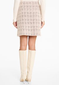 Knielange tweedrok in lichtroze met een gestructureerd ruitpatroon, gedragen met hoge, strakke crèmekleurige laarzen met een spitse neus en stilettohak.