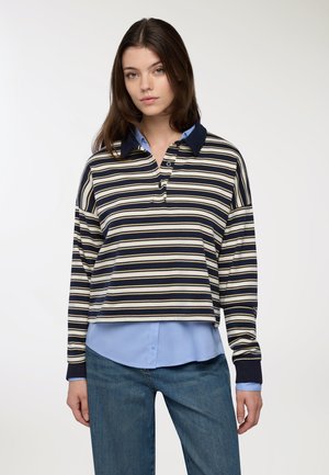 Polo a maniche lunghe a righe in navy, crema e blu. Ha un collo a contrasto, bottoni e un design accorciato. Indossato sopra una camicia azzurro chiaro.
