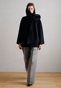 Černý vlněný oděv s nadměrnou kapucí, doplněný světle šedými formálními kalhotami. Vyznačuje se volným střihem a minimalistickým designem.