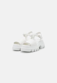 White platform sandals featuring a chunky sole, open-toe design, and adjustable ankle straps. Smooth texture with minimal detailing.