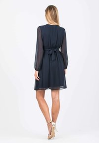 Marineblaues Kleid mit langen durchsichtigen Ärmeln, gerafftem Taillenzug und einem Bindegürtel. Glatte Textur, knielanges Design und eine fließende Silhouette.