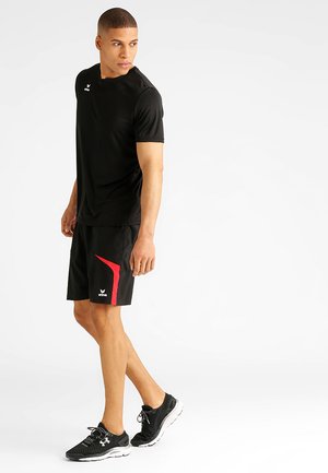 T-shirt de sport noir à manches courtes, associé à un short noir avec une touche de rouge. Porté avec des baskets noires et blanches.