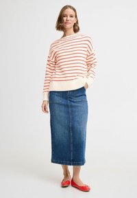 Gestreepte gebreide trui in crème en rood, gecombineerd met een blauwe denim maxi-rok. Rode platte schoenen maken de outfit compleet. Soepele textuur, relaxte pasvorm.