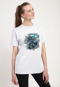 Bílý bavlněný tričko s barevným grafikou skateboardisty v modrém oblečení, umístěné na stylizovaném šedém pozadí.