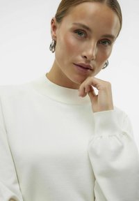 Pull blanc à manches longues avec un col côtelé haut et des manches bouffantes. Texture lisse, design simple et silhouette ajustée.