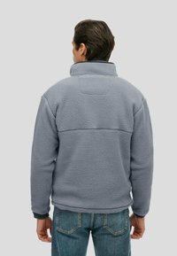 Grijze fleecjas met een hoge kraag, gestructureerde stof en geribde manchetten. Beschikt over een schouderpaneelontwerp op de rug en heeft een losse pasvorm.