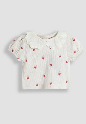 Biele krátke rukávy košele s lemovaným čipkovým golierom, zdobené malými červenými jahodovými vzormi. Mäkka, textúrovaná tkanina so slabými záhybmi.