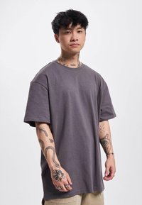 Løs pasform, kortærmet, mørkegrå T-shirt lavet af bomuld. Har en ribbet halsudskæring og en glat tekstur.