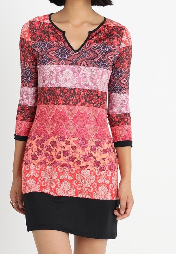 Femme portant une robe colorée à motifs avec des manches trois-quarts et un ourlet noir ajusté sur fond blanc.